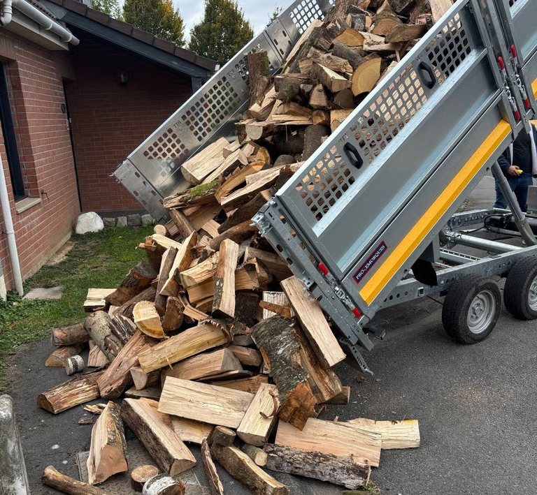 Remorque basculante déchargeant des bûches de bois de chauffage devant une maison